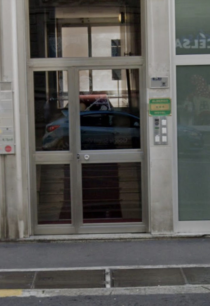 Ingresso a vetri di un hotel tre stelle con citofono, senza rampa visibile per l'accesso dalla strada