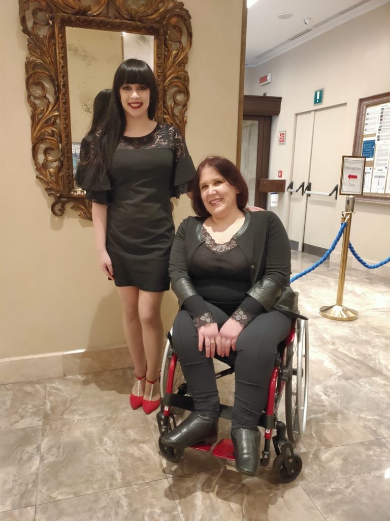 Due donne eleganti in un hotel, una in piedi e una su una carrozzina, vicino a uno specchio decorato